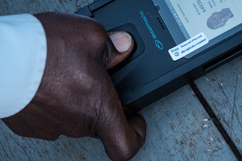 A man puts his thumb on a biometric machine to check his ID to cast his vote at a polling station in Kampala